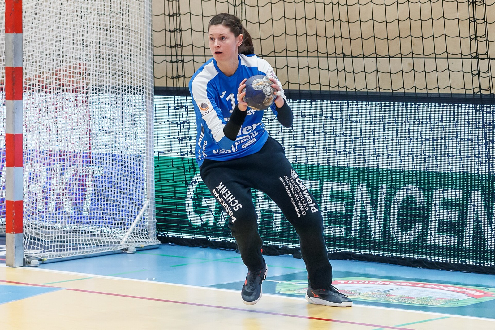 Handball-Torhüterin steht mit dem Ball in beiden Händen im Tor und blickt konzentriert ins Spielfeld